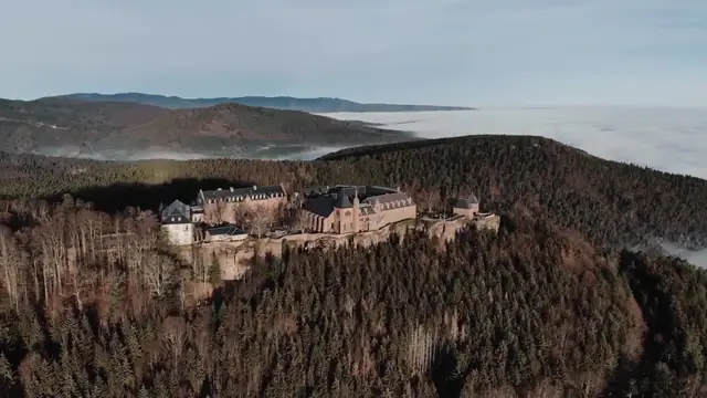 Vue aérienne d'un château sur une colline boisée au-dessus d'une mer de nuages