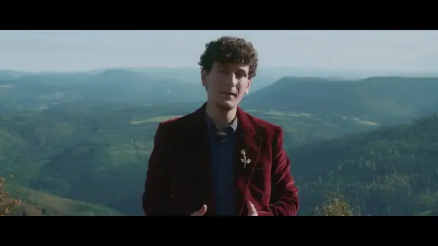 Un jeune homme en veste de velours rouge devant un paysage de collines